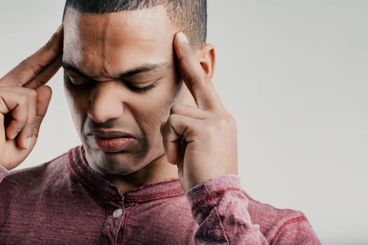 Individual with a strained expression, fingers pressed to his temples. Wearing a maroon shirt, he looks to be in pain, possibly from a headache or severe stress, conveying frustration and discomfort