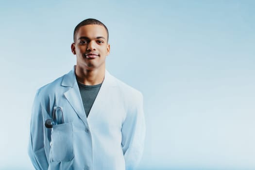 Young doctor with a confident smile, wearing a white lab coat and a stethoscope in the pocket. His professional demeanor and calm expression reflect competence and approachability