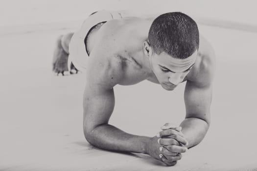 Muscular man performing a plank exercise on a wooden floor, old-skool strength and endurance. His focused expression and clenched hands emphasize determination and physical effort