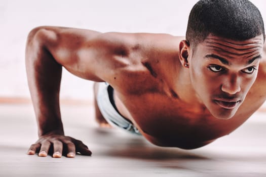 Determined young man, in the midst of push-ups, showing off a strong, muscular body. His short hair and focused expression emphasize his commitment to fitness and strength training