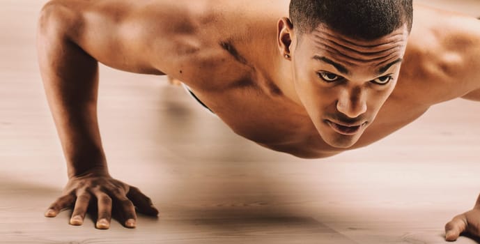 Individual with short hair, performing push-ups with a concentrated expression. His muscular build and intense gaze reflect his dedication to physical fitness and rigorous exercise