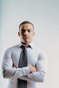 Young man with a serious expression, dressed in a white shirt and patterned tie, arms crossed. His posture and formal attire convey confidence and professionalism, indicating readiness for business