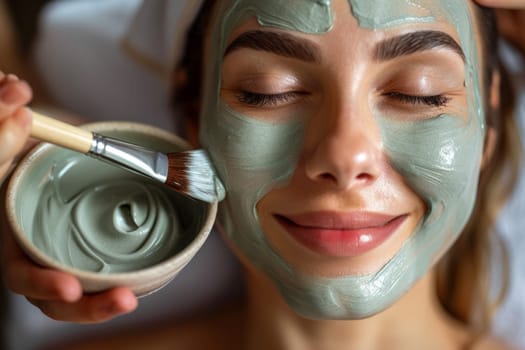 Close up of hands holding bowl with green face mask and brush. Beauty and skin care concept in beauty salon