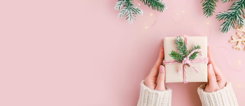 Christmas holiday holding a little gift box with ribbon and fir branch, greeting card, pink pastel background
