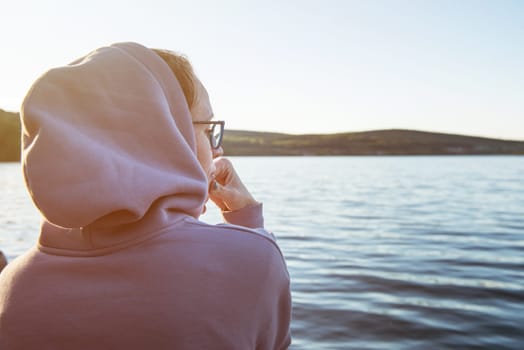 Young beautiful woman sitting on the pier with copy space, summer sunset