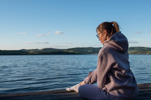 Young beautiful woman sitting on the pier with copy space, summer sunset
