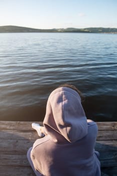 Young beautiful woman sitting on the pier with copy space, summer sunset