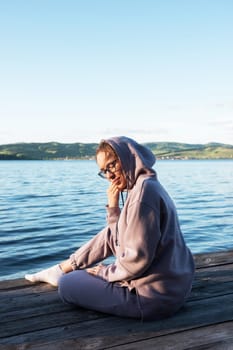 Young beautiful woman sitting on the pier with copy space, summer sunset