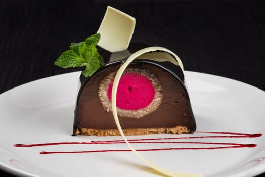 Delicious biscuit chocolate cake closeup with pink souffle decorated with mint and white chocolate on dark background