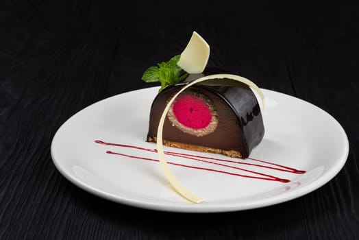 Delicious biscuit chocolate cake closeup with pink souffle decorated with mint and white chocolate on dark background