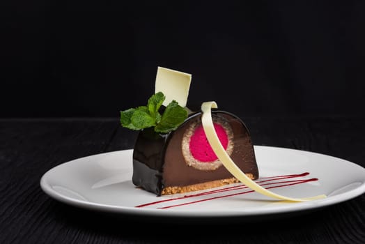 Delicious biscuit chocolate cake closeup with pink souffle decorated with mint and white chocolate on dark background