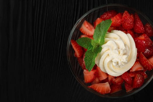 Strawberry with cream decorated with mint leaf on black wooden background, with copyspace, food and drink concept