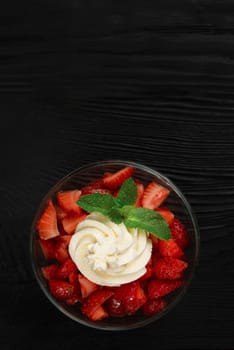 Strawberry with cream decorated with mint leaf on black wooden background, with copyspace, food and drink concept