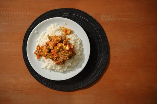 Overhead view of spicy chicken stew with vegetables and rice on wooden background