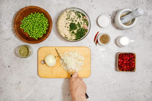 Unrecognizable man cutting fresh onion on wooden chopping board, top view