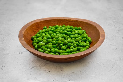 Thawed fresh green peas in a wooden bowl on a grey stone table