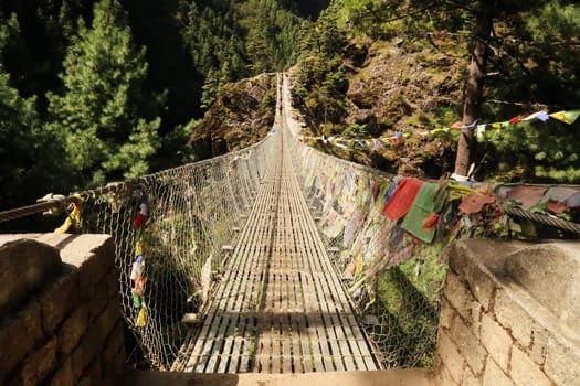 The famous Hillary bridge, a long metal suspension bridge between Phakding and Namche Bazar, Bazaar, covered in many colorful prayer flags, Mount Everest Basecamp Trek, EBC, Nepal 2022