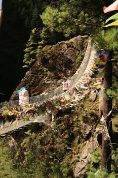 Porters with heavy loads are crossing the Hillary suspension bridge between Phakding and Namche Bazar, Bazaar, the colorful prayer flags attached to it ar moving in the wind, Mount Everest Basecamp Trek, EBC, Nepal 2022