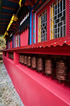 The colorful facade of the monastery in Monjo, Manjo village with a row of copper prayer wheels, Mount Everest Basecamp Trek, EBC, Nepal 2022