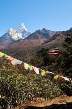 View onto the monastery of the Tengboche village with a prayer flag in the foreground and the peak of Mount Ama Dablam in the background, Mount Everest Base Camp Trek, EBC, Nepal 2022