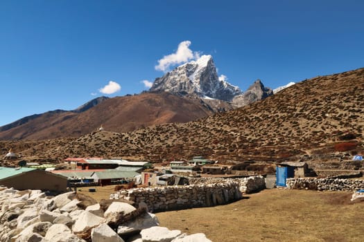 Walking through dingboche village, houses with stone walls in the foreground, two pagodas in front of the peak of Mount Tobuche in the background, Mount Everest Base Camp Trek, EBC, Nepal 2022
