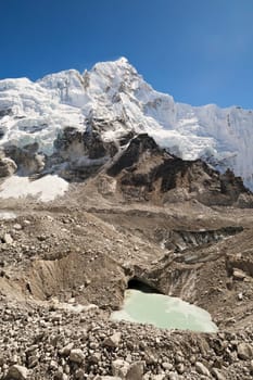 View up to the snow covered peak of Mount Nuptse, from the Khumbu Glacier with a little pond, hole filled with green melt water in the foreground, Mount Everest Base Camp Trek, EBC, Nepal 2022