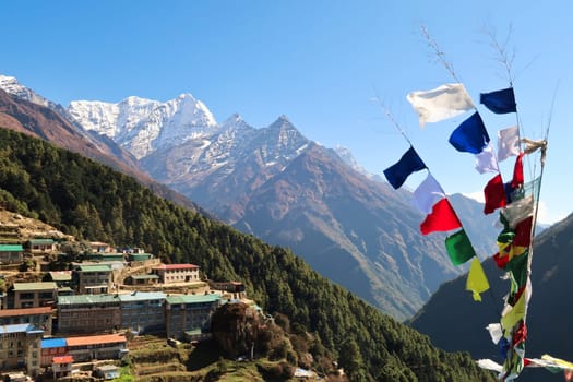 View onto a neighborhood of Namche Bazaar, Bazar with colorful prayer flags next to it and Mount Kusum Kanguru, Kangguru in the background, Mount Everest Base Camp Trek, EBC, Nepal 2022