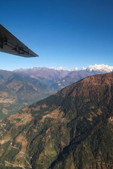View out of the window on the flight from Lukla back to Kathmandu, a mountain with trails in front of snow capped peaks of the Himalayas, Mount Everest Base Camp Trek, EBC, Nepal 2022