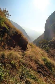 Narrow trail running, winding along a steep hill with dense vegetation above the valley, canyon of the Marsyangdi River, close to Chamje, Chamche village Annapurna Circuit Trek, Nepal 2022