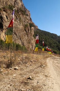 Many colorful flags, prayer flags on poles, flagpoles lined up along the road, trail outside of Bhratang, Bratang village, Annapurna Circuit Trek, Nepal