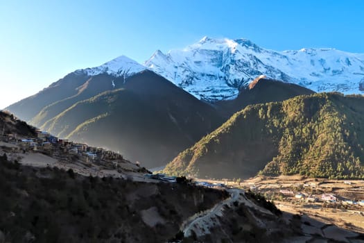 View onto the villages of Upper Pisang and Lower Pisang in front of Annapurna II, IV in the early morning, Upper Pisang is still in the shade while Lower Pisang is in the sun, Annapurna Circuit Trek, Nepal 2022
