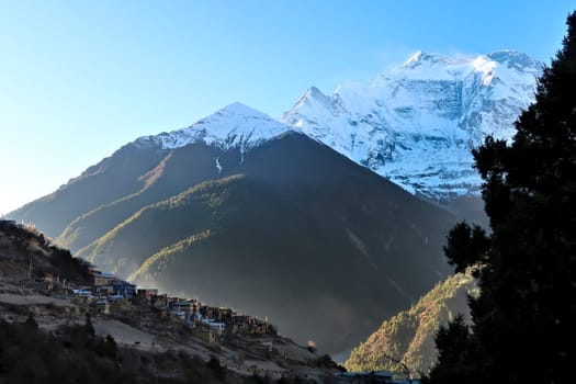 Leaving the village of Upper Pisang in the early morning, the sun shines onto Annapurna II and into the valley while the village is still in the shade, Annapurna Circuit Trek, Nepal 2022