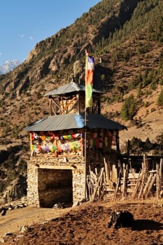 Entrance gate, stupa into Upper Pisang, coming from Lower Pisang, decorated with colorful prayer flags, a cow resting in the foreground, Annapurna Circuit Trek, Nepal 2022