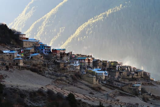 View onto the village of Upper Pisang in the early morning, the village is still in the shade while the valley in the background is illuminated by sunlight, Annapurna Circuit Trek, Nepal 2022