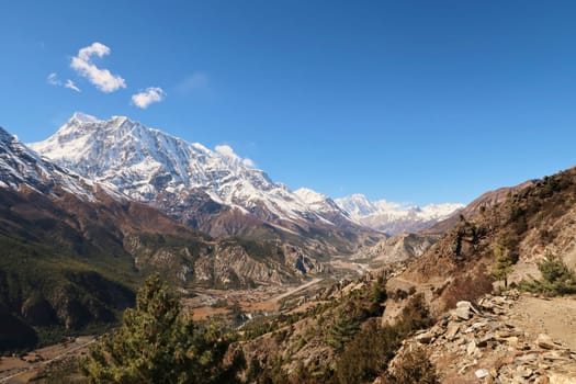 On the trail from Upper Pisang, Ghyaru village to Manang, the snow capped peak of Annapurna III is rising behind the town, airport, landing strip of Manang, Annapurna Circuit Trek, Nepal 2022