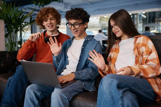 Team of teenagers sitting on sofa in office. Three young employees discussing new work project