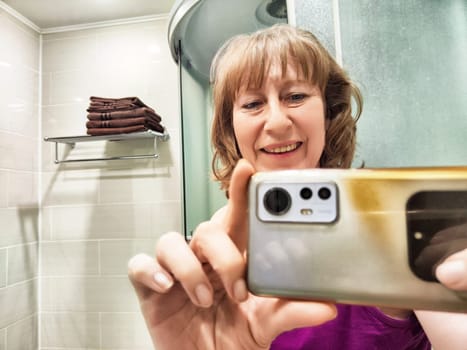 A middle-aged blonde blogger snaps a morning selfie in her bathroom, smiling in the mirror.