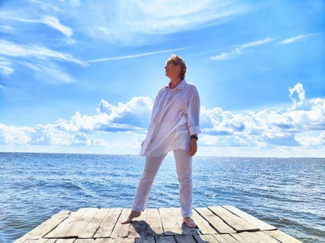 Mature traveler stands on a dock, embracing the sunny skies and ocean breeze while capturing a moment of joy.