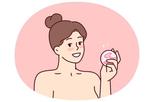 Woman with bath bomb in hands smiles as she prepares to take bath with aromatic substances. Happy girl with bare shoulders demonstrates bomb for comfortable water treatments or SPA