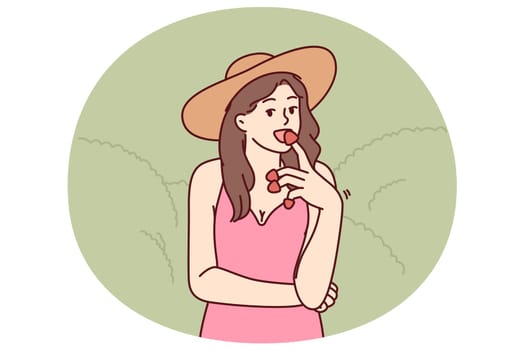 Woman eats appetizing strawberries enjoying taste of fresh berries found on farm or plantation. Girl in hat who owns farm tries organic strawberries grown without use of pesticides