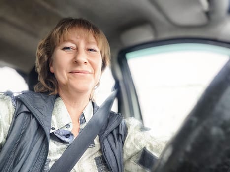 A middle-aged woman smiles while driving her car on an adventure-filled road trip, embracing the journey ahead.