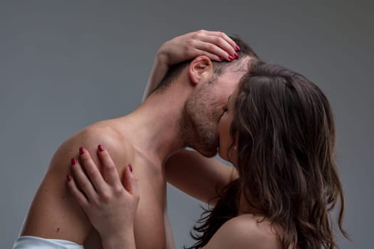 Young couple passionately kissing in a close up shot, showing love and intimacy. Woman's red nails contrast against man's bare chest. Brown hair frames their faces, exuding closeness