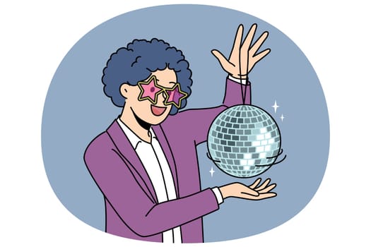 Funny man with disco ball with curly wig on head came to nightclub or dance floor to have fun and relax. Young guy enjoys atmosphere of music festival or disco party for party people