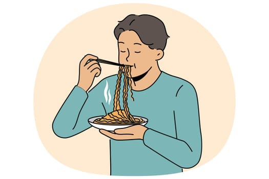 Asian man eats ramen with chinese sticks, enjoying taste of traditional national meal from korean cuisine restaurant. Guy stands and enjoys eating ramen or noodles to get enough during work break