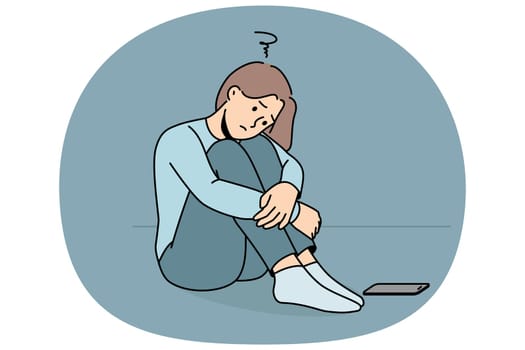 Sad woman is waiting for phone call, sitting on floor and suffering from loneliness or lack of friends. Sad girl sadly awaits arrival of sms message about replenishing bank account