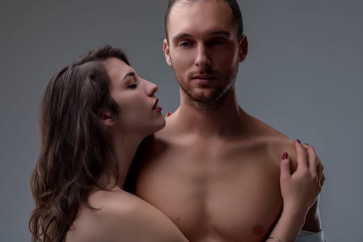 Dark-haired woman displays intense desire, hugging a shirtless, exhausted man. He appears sleepy, reflecting the strain of maintaining the always-ready male stereotype despite his tiredness.