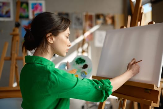 Young woman artist starting to draw on blank empty canvas with oil paints and brush in art studio workshop