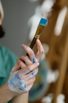 Closeup shot with selective focus on dirty artist hand holding paint brush. Artistic instrument for creating picture at professional art studio workspace