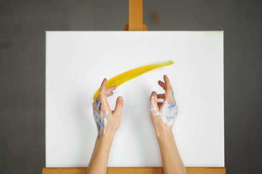Female artist dirty hands over picture canvas making magic move to create beautiful picture drawaing with paints. Art class, therapeutic hobby and artistic education concept