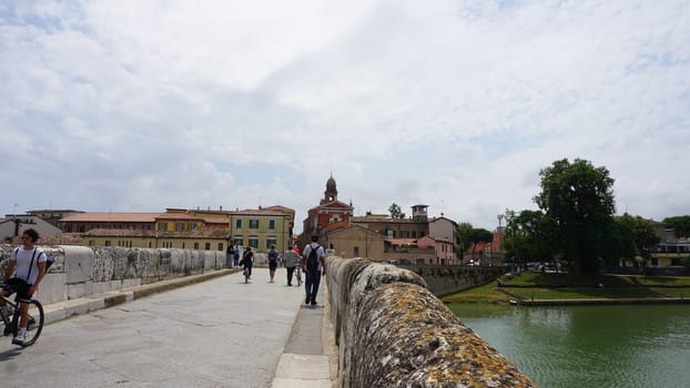 Rimini, Italy - June 25, 2024: People going at Historical roman Tiberius Bridge over Marecchia river in Rimini at Italy